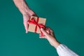 Top view of male and female hands holding a gift box with red ribbon on green background. Royalty Free Stock Photo