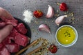 Top view of a male hand taking raw cut meat from a table with garlic cloves, dried pepper, oil