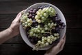 Male hands holding a bowl with red and white grapes on wooden table Royalty Free Stock Photo