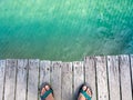 Top view of man feet wearing sandal standing on old wooden bridge over the clean and clear blue sea water. Royalty Free Stock Photo