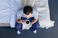 Top view of man in pyjamas holding cup of coffee while sitting on bedding. Royalty Free Stock Photo