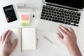 Overhead shot of man working on notebook computer on white desk cluttered with office supplies Royalty Free Stock Photo