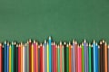 Top view of many, bright multi colored wooden pencils in a row on a dark green background with copy space Royalty Free Stock Photo
