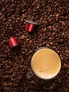 Top view of many roasted coffee beans and glass cup with fresh espresso coffee. Capsules for coffee machines Royalty Free Stock Photo