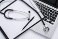 Top view of medical desk with stethoscope, clipboard, pen and laptop