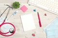 Top view medical workplace with blank notepad, stethoscope, keyboard, thermometer, mask, plant and supplies on white wooden desk