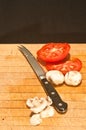 sliced tomato and white mushrooms with a serrated blade, knife on a wood cutting block Royalty Free Stock Photo