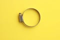 Top view of a metal plumber clamp on a bright yellow background