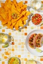 Summer party with mexican food on tile background. Vegetable tacos, nachos, guacamole and salsa sauces with alcoholic