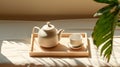 Top view of minimal, beautiful white ceramic teapot, two cups, candle on brown wooden tray on cream tablecloth in sunlight Royalty Free Stock Photo