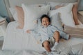 Portrait of afro american joyful little boy on pillows in bed laughing and smiling