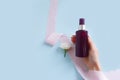 Top view of mock-up of unbranded brown plastic spray bottle, female hand, pink silk ribbon and white flower on a blue background.