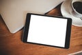 A black tablet pc with blank desktop white screen with laptop and coffee cup on wooden table Royalty Free Stock Photo