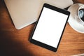 A black tablet pc with blank desktop white screen with laptop and coffee cup on wooden table Royalty Free Stock Photo