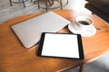 A black tablet pc with blank desktop white screen with laptop and coffee cup on wooden table Royalty Free Stock Photo