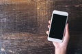 Top view mockup image of hand holding white mobile phone with blank black desktop screen on wooden table Royalty Free Stock Photo