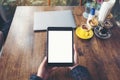 Top view mockup image of hands holding black tablet pc with blank white desktop screen with laptop and coffee cups on wooden table Royalty Free Stock Photo