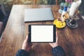Top view mockup image of hands holding black tablet pc with blank white desktop screen with laptop and coffee cups on wooden table Royalty Free Stock Photo