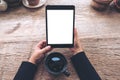 Top view mockup image of hands holding black tablet pc with blank white screen and coffee cup on vintage wooden table Royalty Free Stock Photo