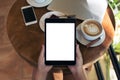 Top view mockup image of hands holding black tablet pc with blank white screen , smart phone , laptop , coffee cup and cake Royalty Free Stock Photo