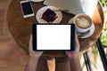 Mockup image of hands holding white mobile phone with blank black screen while eating yellow lemon curd cake on wooden table Royalty Free Stock Photo