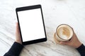 Hands holding black tablet pc with white blank screen and coffee cup on table background Royalty Free Stock Photo