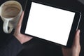 Hands holding black tablet pc with white blank screen and coffee cup on table background Royalty Free Stock Photo