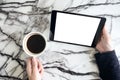 Top view mockup image of hands holding black tablet pc with white blank screen and coffee cup on table Royalty Free Stock Photo
