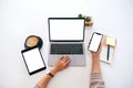 Hands holding a blank white screen mobile phone with laptop computer and tablet pc on the table in office