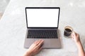 Top view mockup image of hands using laptop with blank white desktop screen and holding coffee cup on marble table Royalty Free Stock Photo