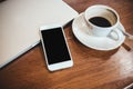 A white mobile phone with blank black desktop screen on a computer laptop with coffee cup Royalty Free Stock Photo