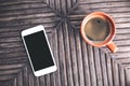 Top view mockup image of a white mobile phone with blank black desktop screen and a cup of coffee on vintage wooden table Royalty Free Stock Photo