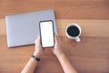 A woman holding and using black mobile phone with blank white desktop screen with coffee cup and laptop Royalty Free Stock Photo