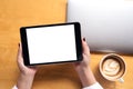 Top view mockup image of woman`s hands holding black tablet pc with white blank screen and laptop , coffee cup on wooden table Royalty Free Stock Photo