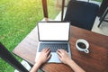 A woman using and typing on laptop with blank white desktop screen and coffee cup on wooden table and green nature background Royalty Free Stock Photo