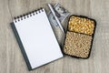 Top view mockup of open blank notebook on spiral, automatic pen. 100 dollar banknotes and samples of soybean and corn seeds,