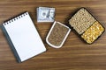 Top view mockup of open blank notebook on spiral, automatic pen. 100 dollar banknotes and samples of soybean, corn and wheat seeds