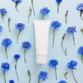 Top view of mockup of white squeeze bottle plastic tube for branding and blue cornflowers on a pastel blue background