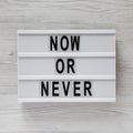 Top view, modern board with text `Now or never` on a white wooden surface. Flat lay, overhead, from above Royalty Free Stock Photo