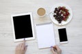 Top view, modern feminine workspace with female hands, smartphone, tablet, notepad, berries and latte on white wooden background. Royalty Free Stock Photo