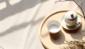 Top view of modern minimal beautiful white ceramic teapot teacup with saucer on brown straw mat wooden tray on cream tablecloth in Royalty Free Stock Photo
