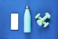 Top view of modern smartphone with blank screen on sports mat with dumbbells and bottle of water. Flat lay, mockup