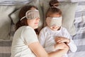 Top view of mother lying on pillow with daughter, wearing blindfolds, resting in morning in bedroom, sleeping hugging in bed, lazy