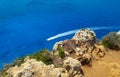 Top view from the mountain to the beautiful blue,clear water with a small boat, and tiny shrubs on rock in foreground Royalty Free Stock Photo