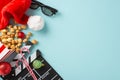 Top view of a movie clapper, 3D glasses, striped popcorn box, Santa\'s hat, baubles, thematic candies on a light blue surface