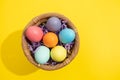 Top view of multi colored Easter eggs in a straw basket on a yellow background Royalty Free Stock Photo