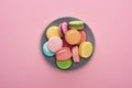 Top view of multicolored delicious French macaroons on plate on pink background.