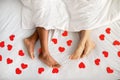 Top view of multiracial couple lying under blanket on bed with red paper hearts, closeup of feet Royalty Free Stock Photo
