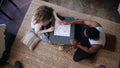 Top view of multiracial couple sitting on floor and playing board game. Woman throws dice, takes card. Man waits turn.