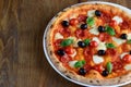 Top view of neapolitan pizza with pepperoni, mozzarella, cherry tomatoes and black olives on a wooden table. Close up. Macro.